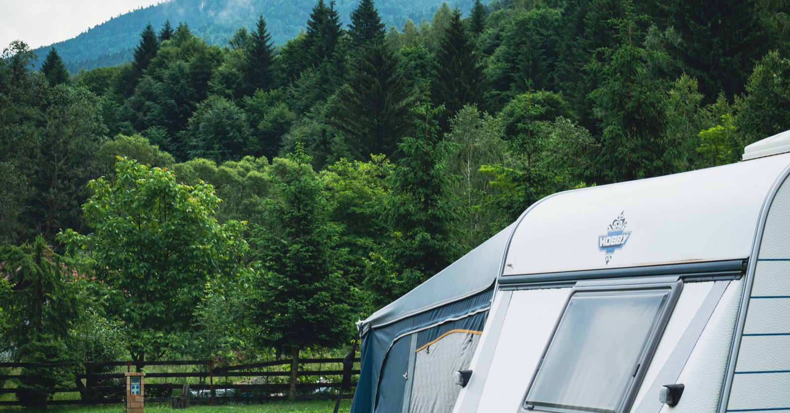 Caravana acampada en una parcela de un camping rodeada de bosque y montaña