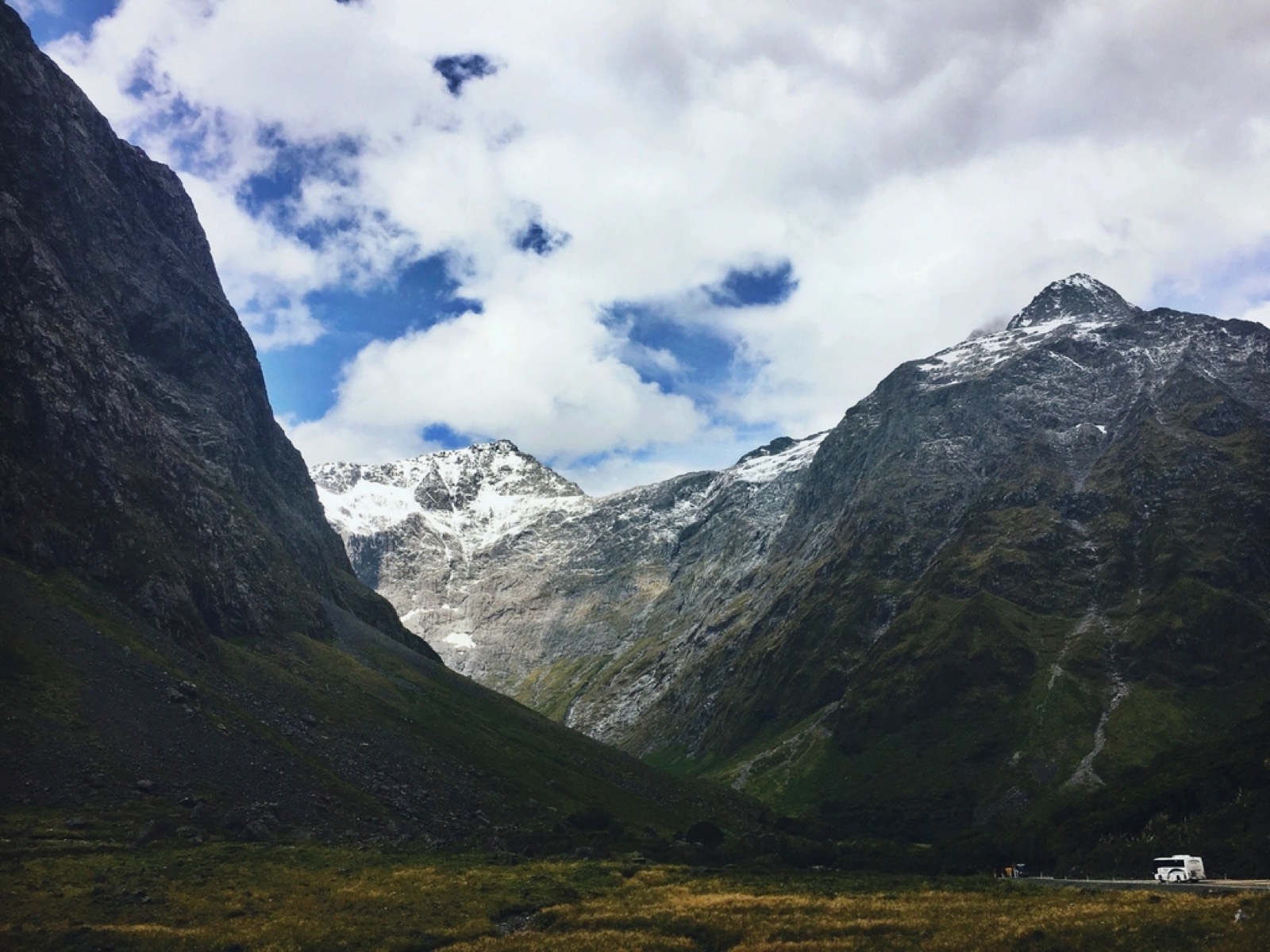 Carretera de montaña entre cumbres nevadas con una autocaravana al fondo